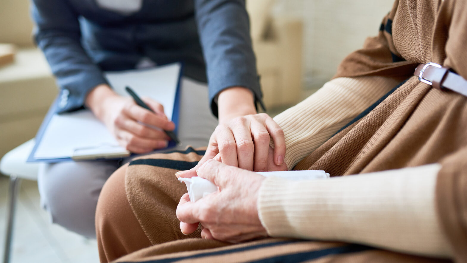 Close up of female psychologist holding hand of senior woman during therapy session